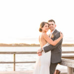 Wedding at Blithewold Mansion, Gardens & Arboretum in Bristol RI. Bride and groom embracing on a dock by the water at sunset.