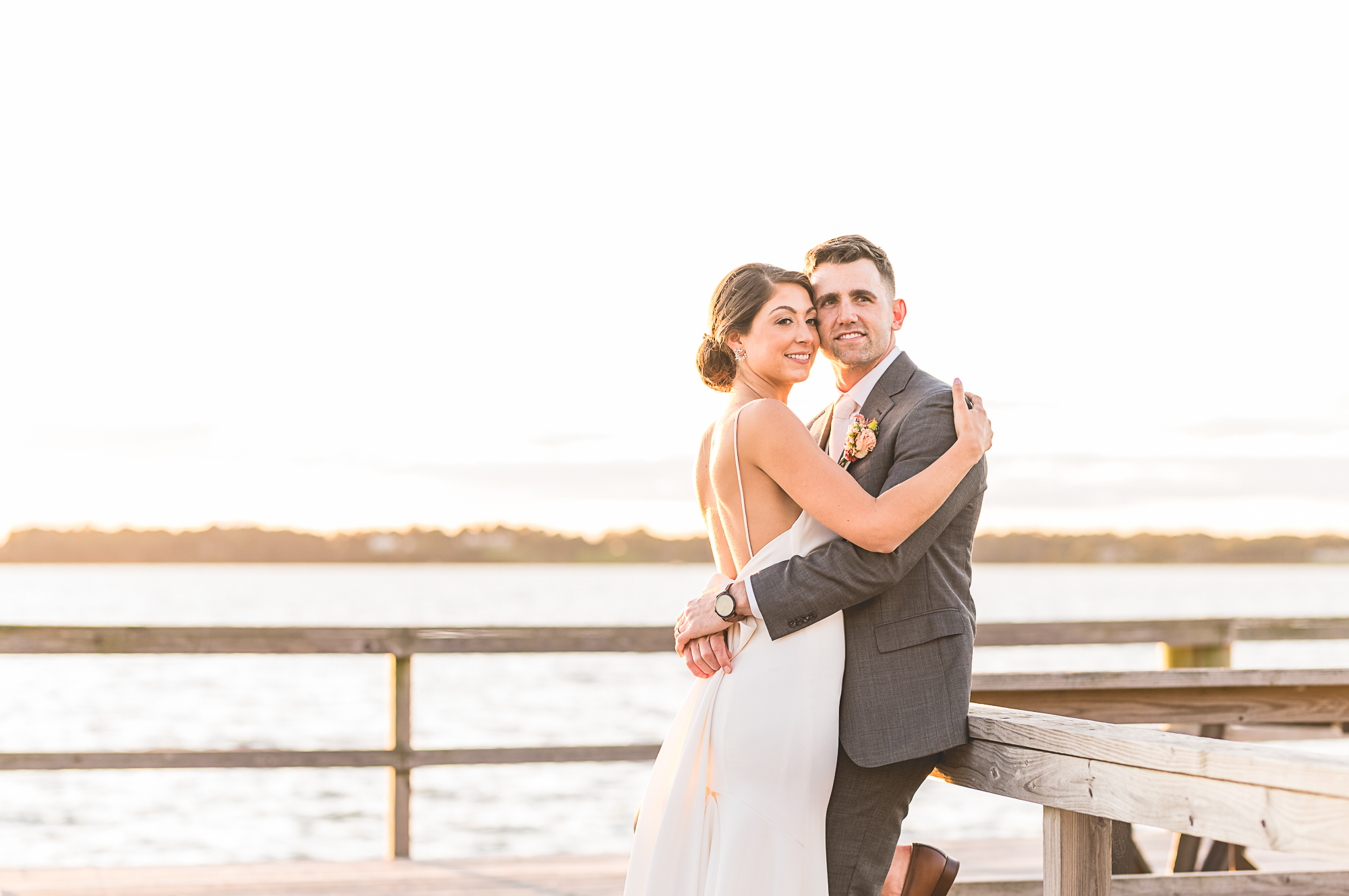 Wedding at Blithewold Mansion, Gardens & Arboretum in Bristol RI. Bride and groom embracing on a dock by the water at sunset.